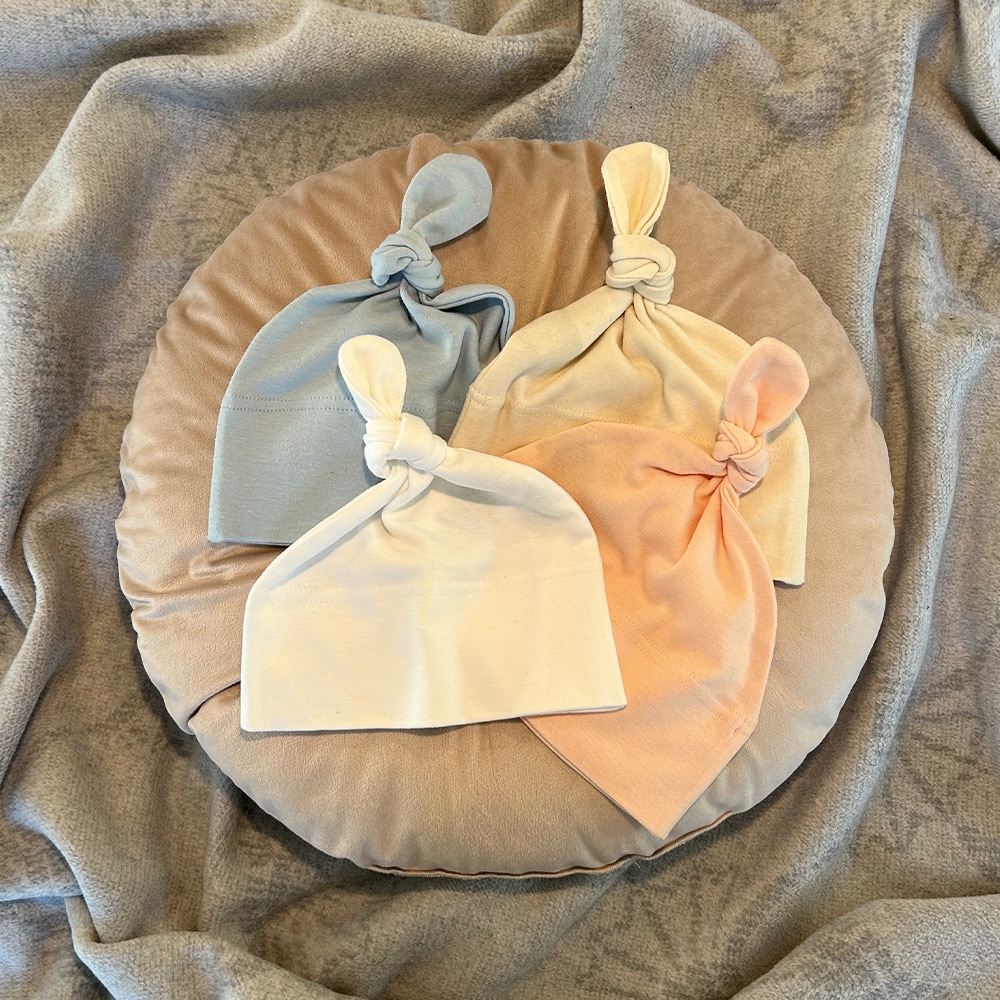 Süße Bio-Baumwoll-Babymütze mit Knoten in den Farben blau, rosa, weiß und natur.